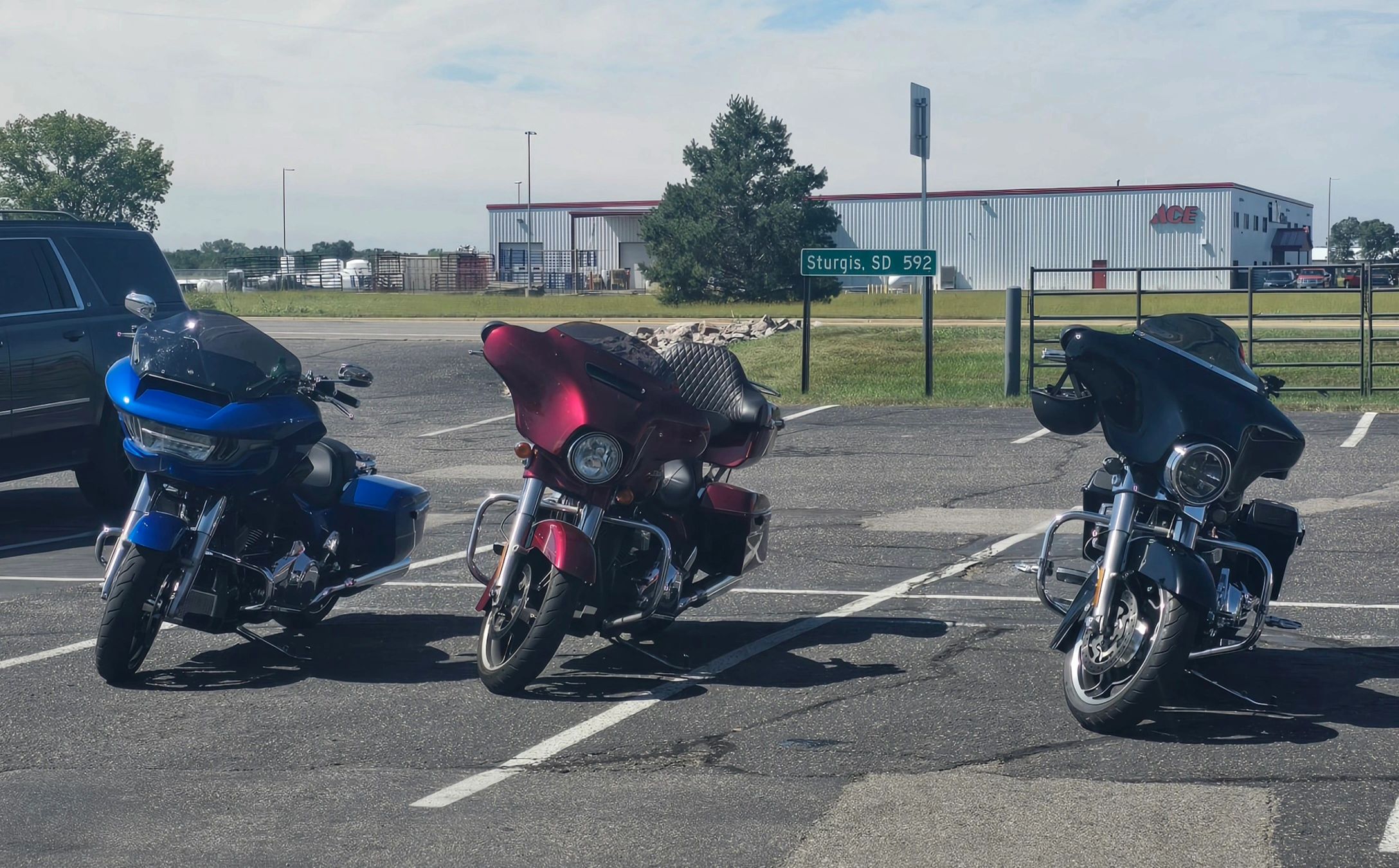 Three motorcycles parked in a lot near an Ace Hardware building.