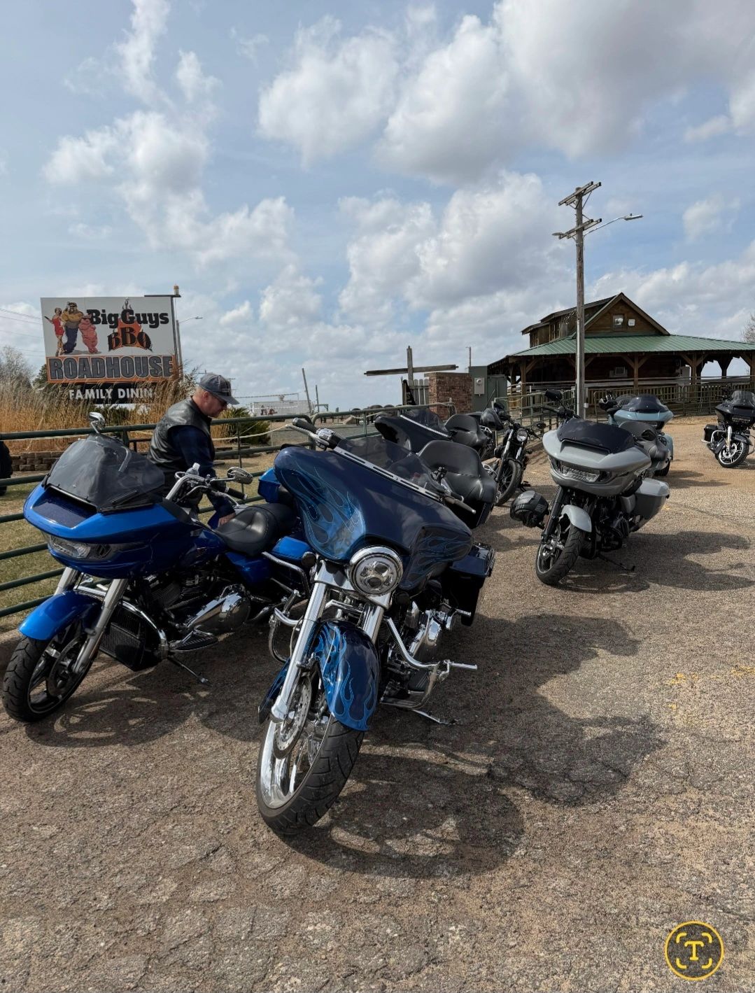 Group of motorcycles parked outside a roadhouse with a man adjusting one bike.