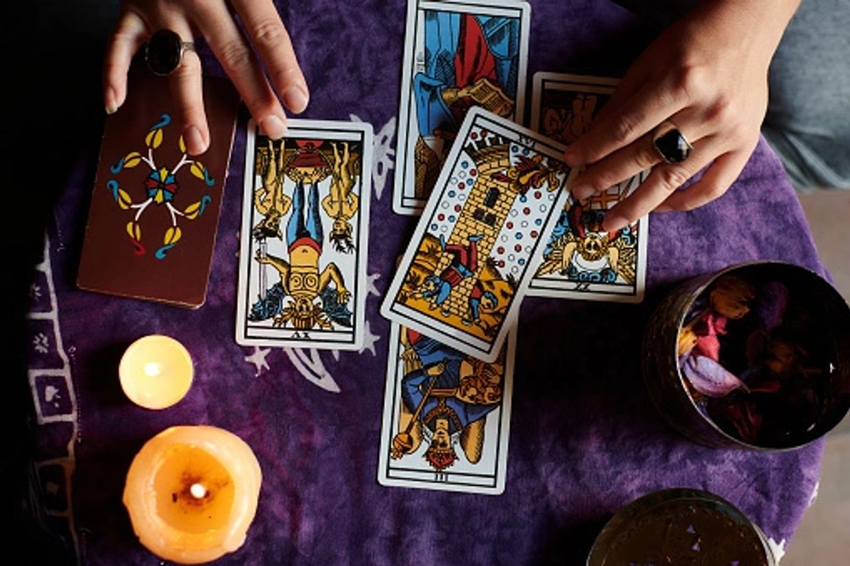 Hands reading tarot cards with candles and a bowl of petals nearby.