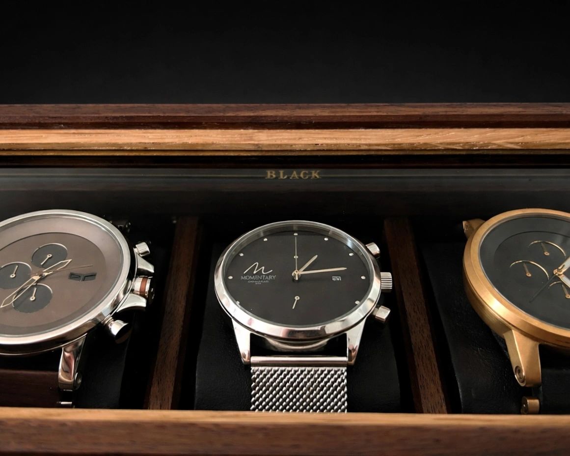 Three luxury wristwatches in a wooden display box.