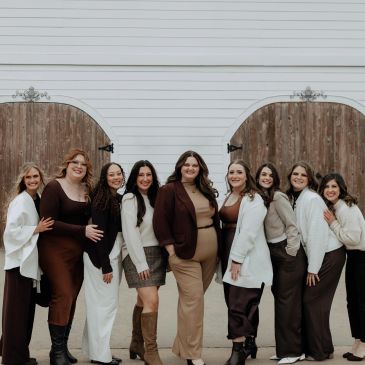 A group of nine women standing together, dressed in coordinated neutral and brown tones.