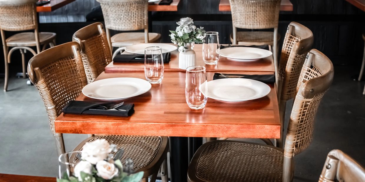 A neatly set wooden dining table with plates, glasses, and black napkins.