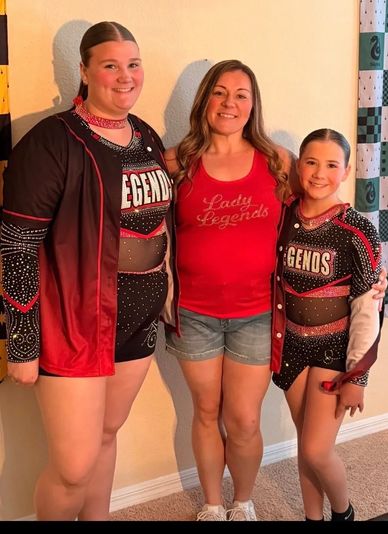 Three smiling females, two in cheerleading outfits.