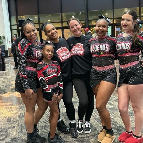 Group of cheerleaders and coaches smiling indoors.