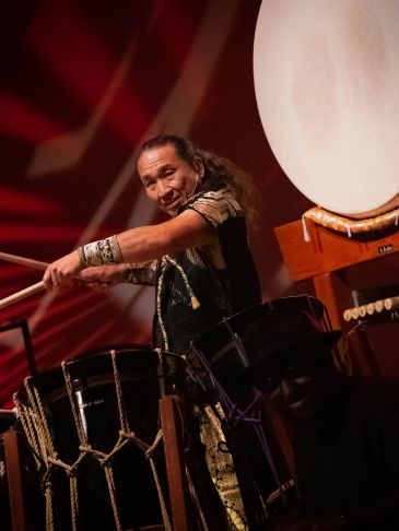 Man energetically playing traditional drums on stage.