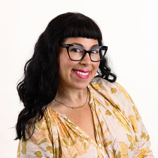 Smiling woman with black hair, cat-eye glasses, and floral blouse.