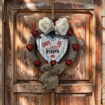 Rustic heart-shaped wreath with love-themed decorations on a weathered wooden door.