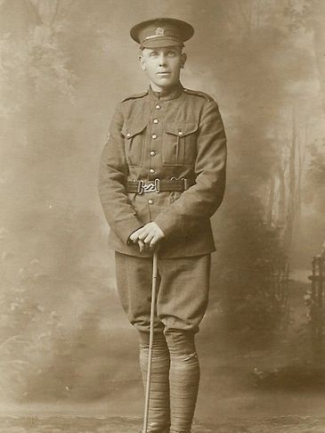 A young soldier in vintage military uniform stands holding a cane.