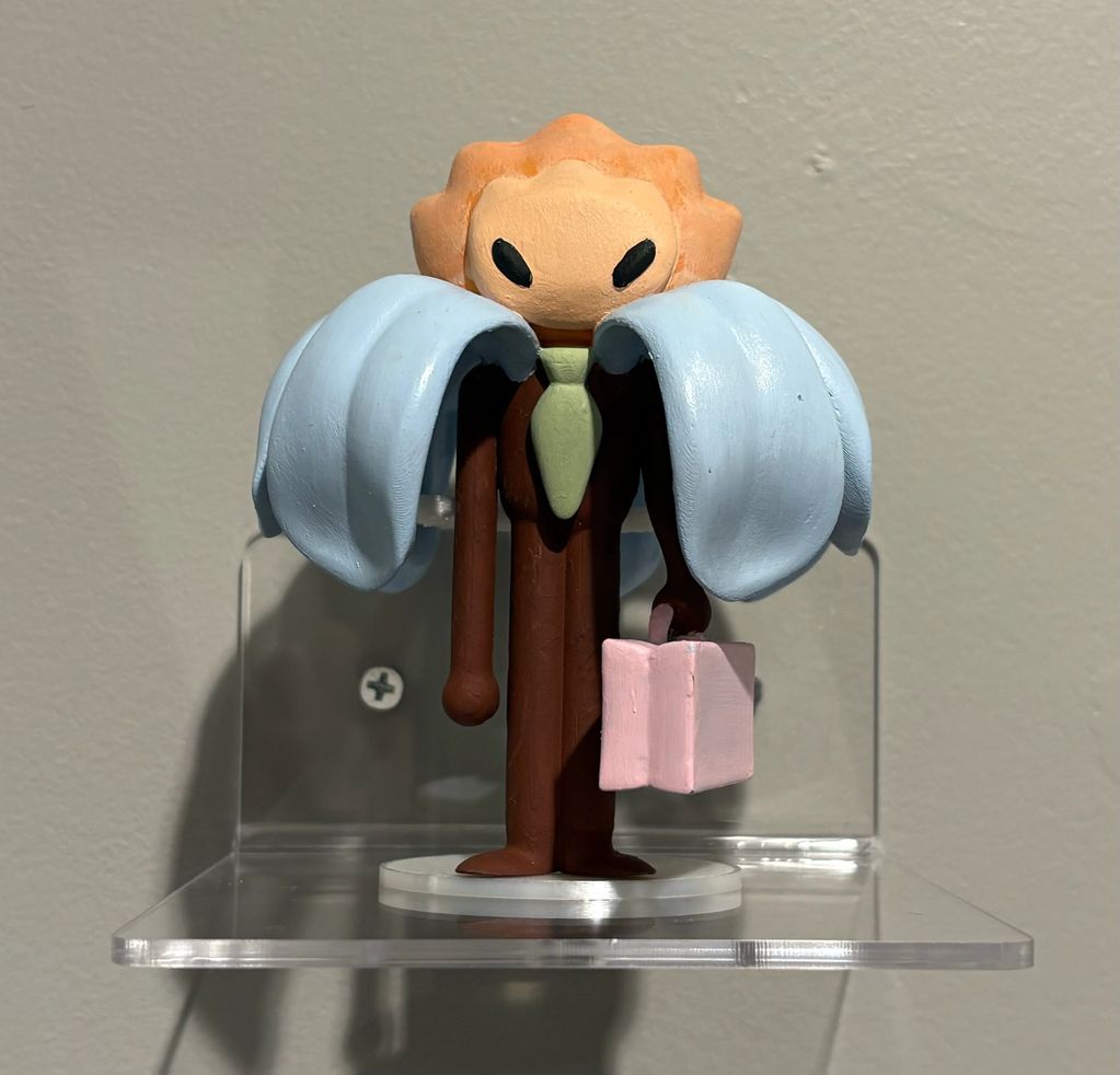 A stylized figurine with blue wings and a pink briefcase stands on a clear shelf.