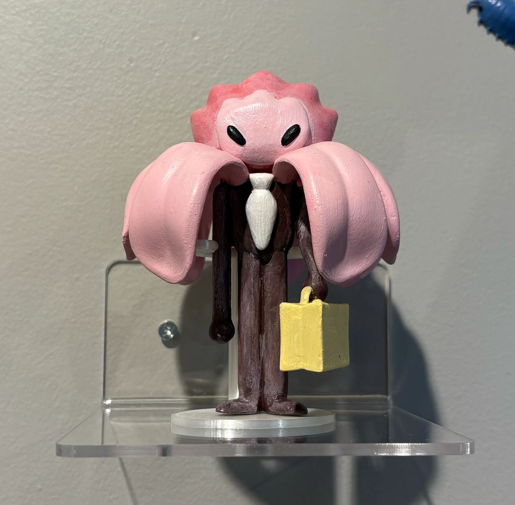 A figurine with a pink flower head, black eyes, wearing a suit and holding a yellow briefcase.