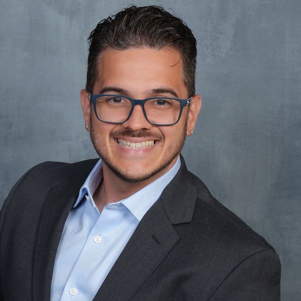 Smiling man in glasses and suit jacket against a gray background.