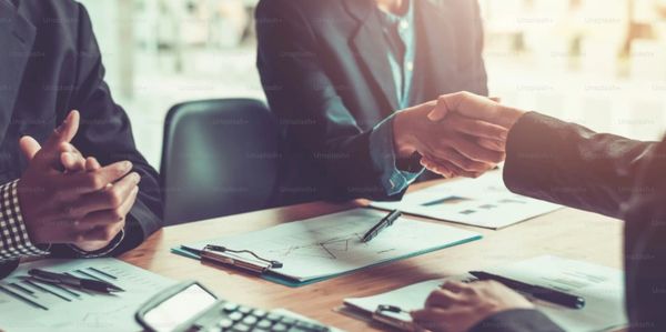 Two business professionals shaking hands over a desk with documents and a calculator.