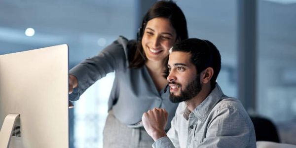 Two colleagues collaborating and smiling while looking at a computer screen.