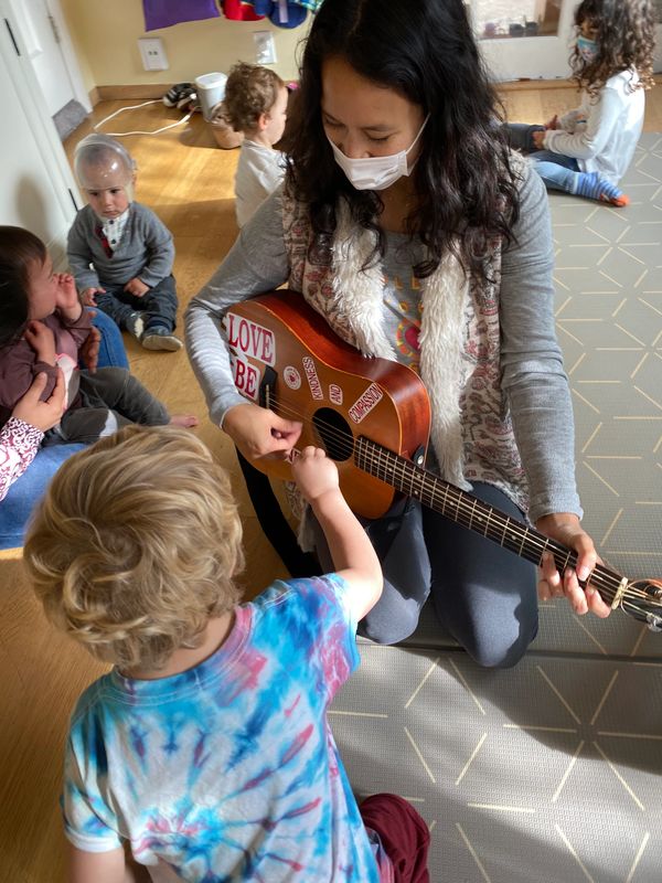 A group of children surrounded by Ms. Dani, our music instructor who is playing a guitar for the chi