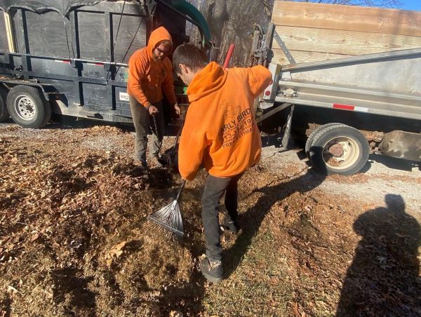 Two people raking leaves outside on a sunny day.