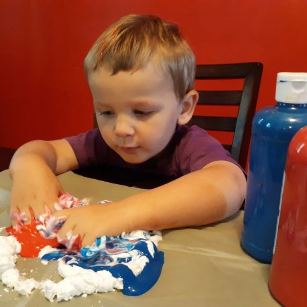 A young boy playing with colorful paint and foam on a table.