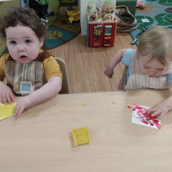 Two toddlers engaged in finger painting at a table.