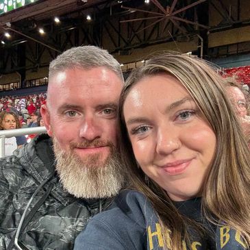 A smiling couple taking a close-up selfie at an indoor event.