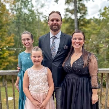 A family of four dressed elegantly outdoors, smiling at the camera.