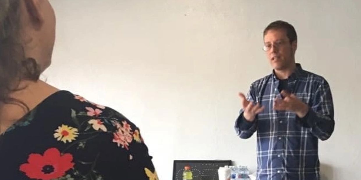A man in glasses explains something to a woman wearing a floral top.