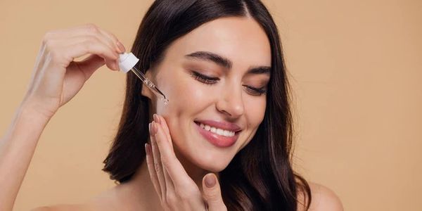 Woman applying facial serum with a dropper, smiling gently.