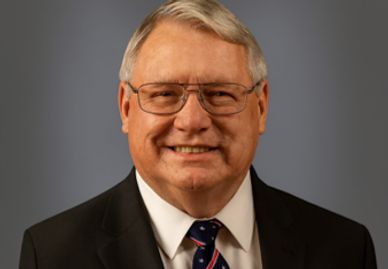 Portrait of an older man with glasses in a suit and tie, smiling.