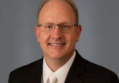 A middle-aged man in a suit and glasses smiling.