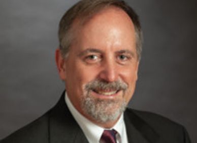 Professional headshot of a middle-aged man in a suit and tie.