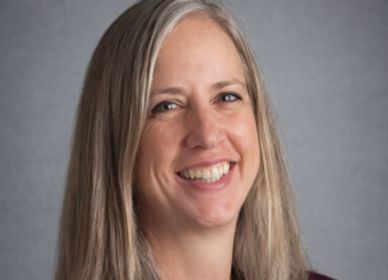 Smiling woman with long blonde hair against a gray background.