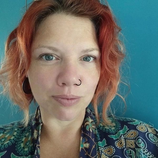A picture of Jody a red headed, curly haired woman with a nose piercing.