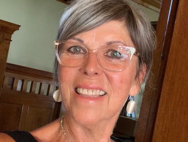 Smiling woman with short gray hair and glasses indoors.