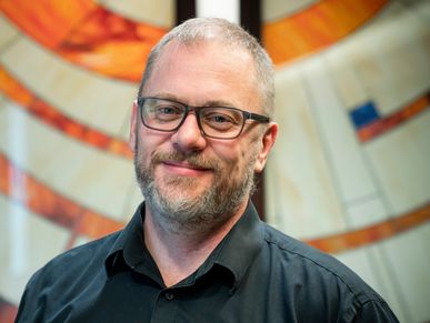 Smiling man with glasses and beard in front of colorful abstract background.
