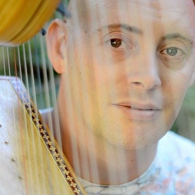 Man playing a harp with focus on his face and harp strings.