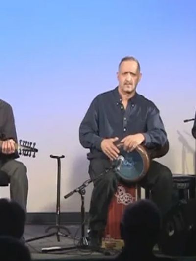 A man playing a goblet drum on stage with a blue background.