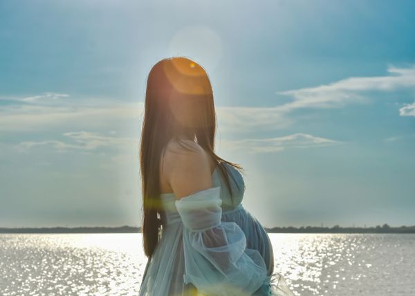 Lake sunset scenery. Pregnant woman holding bump, gazing at sunset. Solar flare over left profile