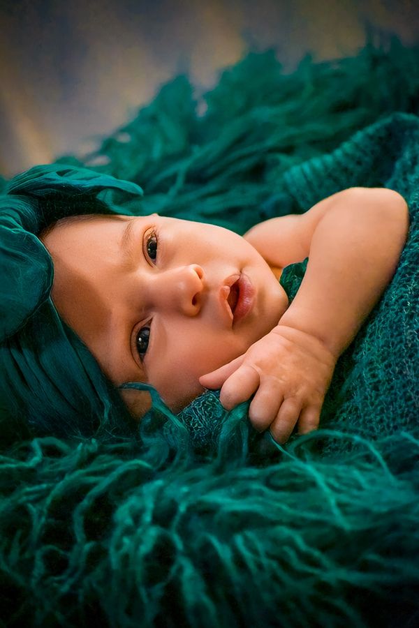 Newborn, wearing teal headband and wrap. Posed with one arm out, soft focus.