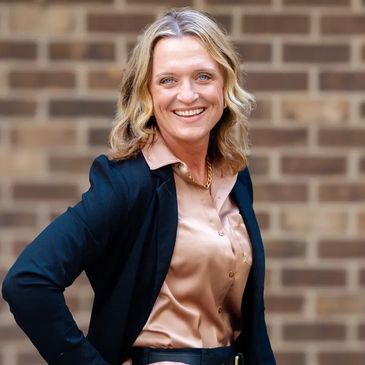 Confident woman smiling in professional attire against a brick wall.