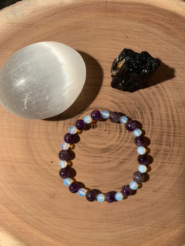 A beaded bracelet with purple and translucent stones on a wooden surface, next to two crystals.