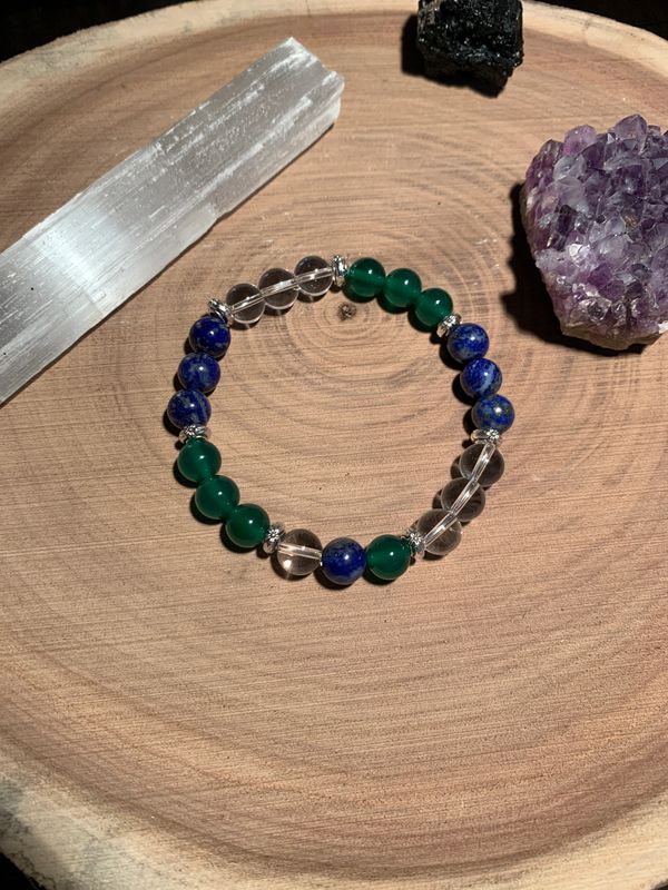 Beaded bracelet with blue, green, and clear stones on a wooden surface with crystals.