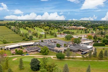 Aerial view of a golf course and clubhouse surrounded by trees and farmland.