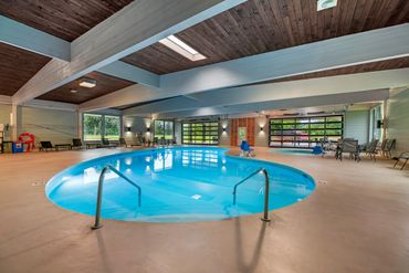 Indoor swimming pool with seating and large windows overlooking greenery.