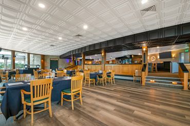 Spacious restaurant dining area with wooden chairs and black tablecloths.