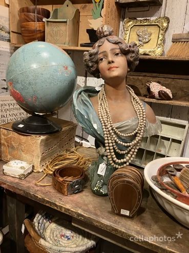 Antique bust with pearl necklaces beside a globe and vintage items on a wooden table.