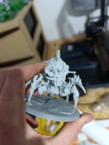 Unpainted miniature model of an insect-like creature held in hand.