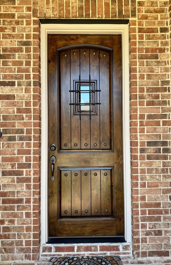 Elegant wooden door with iron grill and brick wall frame.