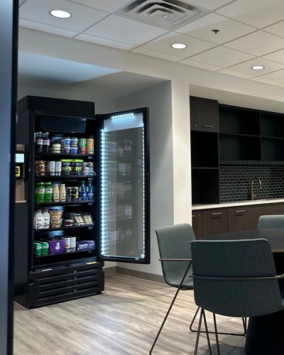 Office kitchen area with open refrigerator stocked with snacks and drinks.