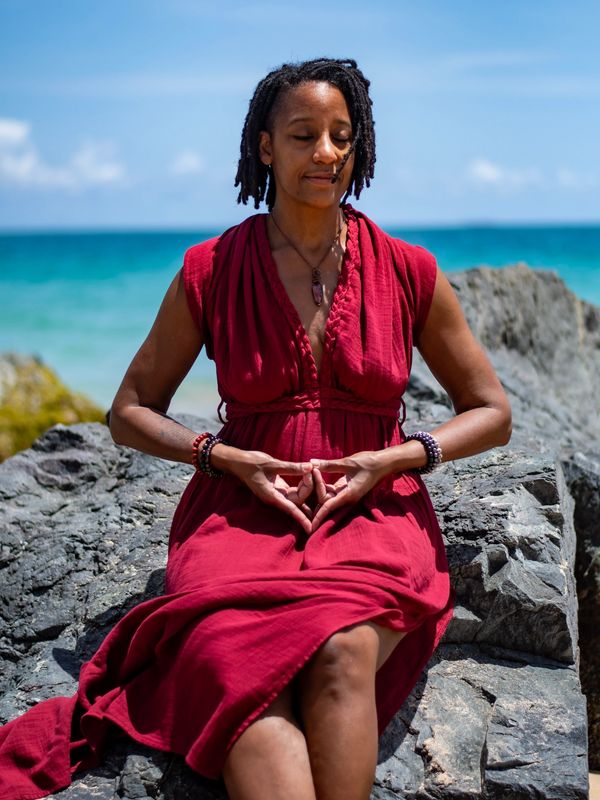 Woman meditating on rocks by the ocean in red dress.