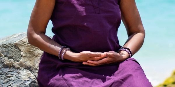 Person meditating by the water in purple clothing.