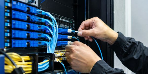 Hands connecting blue fiber optic cables to a network panel.