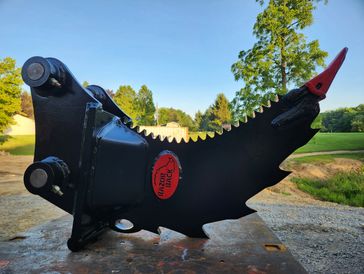 Black excavator attachment with sharp teeth and red tip.